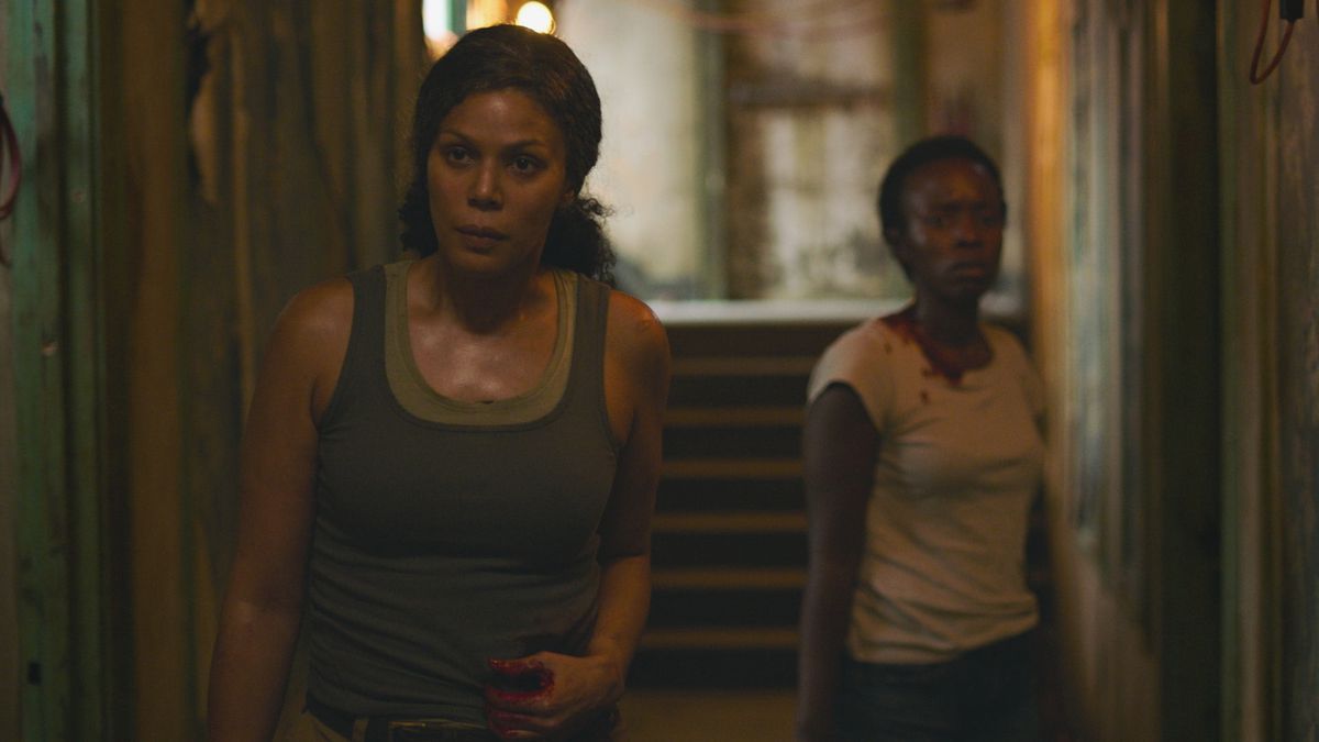 Marlene and Kim, two Fireflies, stand injured in a dim hallway facing the camera in the HBO series The Last of Us