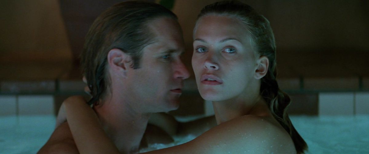 Natasha Henstridge looks into the distance while hugging a man in a pool in Species