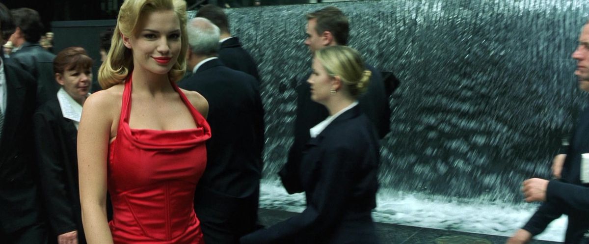 Fiona Johnson smiles while looking into the camera and wearing a red dress in The Matrix