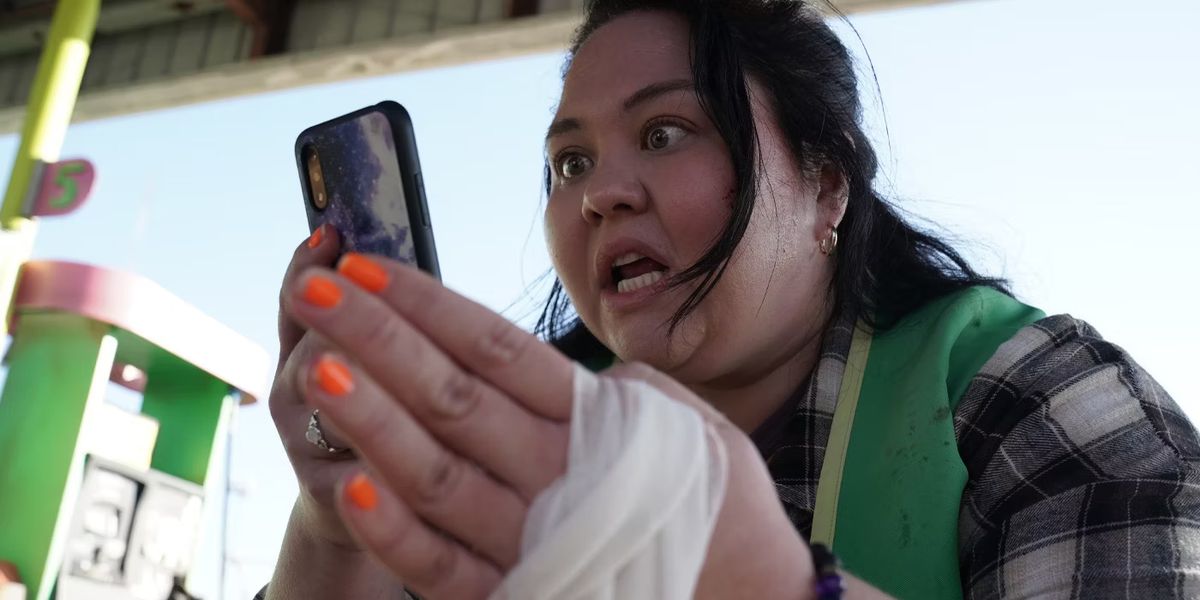 A woman (Jolene Purdy) stares distressingly at a cell phone with a bandaged hand.
