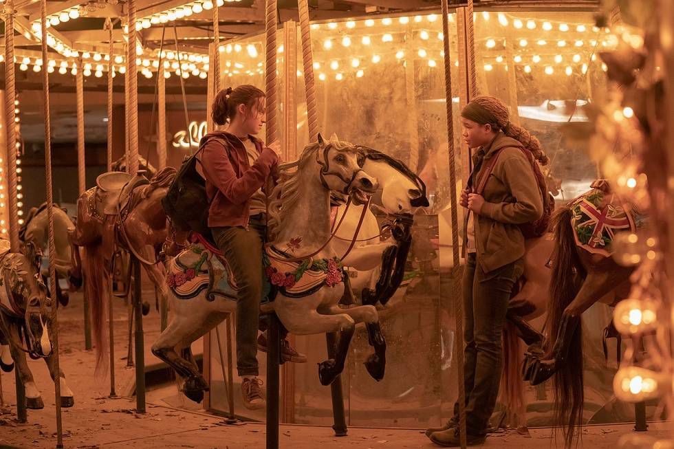 Ellie (Bella Ramsey) sitting on a carousel horse and talking to Riley (Storm Reid)