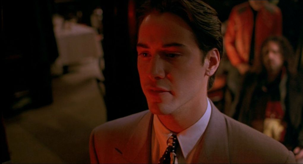 Keanu Reeves wears a beige suit and is front lit by red light in My Own Private Idaho.
