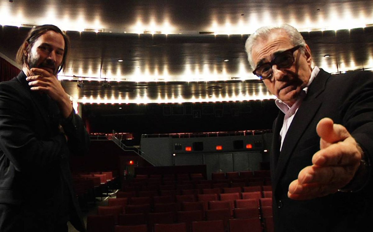 Keanu Reeves with long hair holds his left hand under his chin in an empty auditorium, as Martin Scorsese looks at and gestures to the camera in Side by Side.