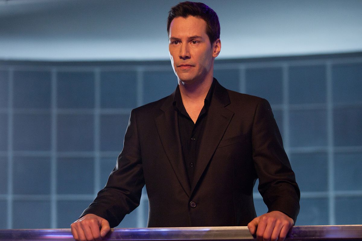 Keanu Reeves, with short hair and wearing a black suit, rests his hands against a railing in Man of Tai Chi.