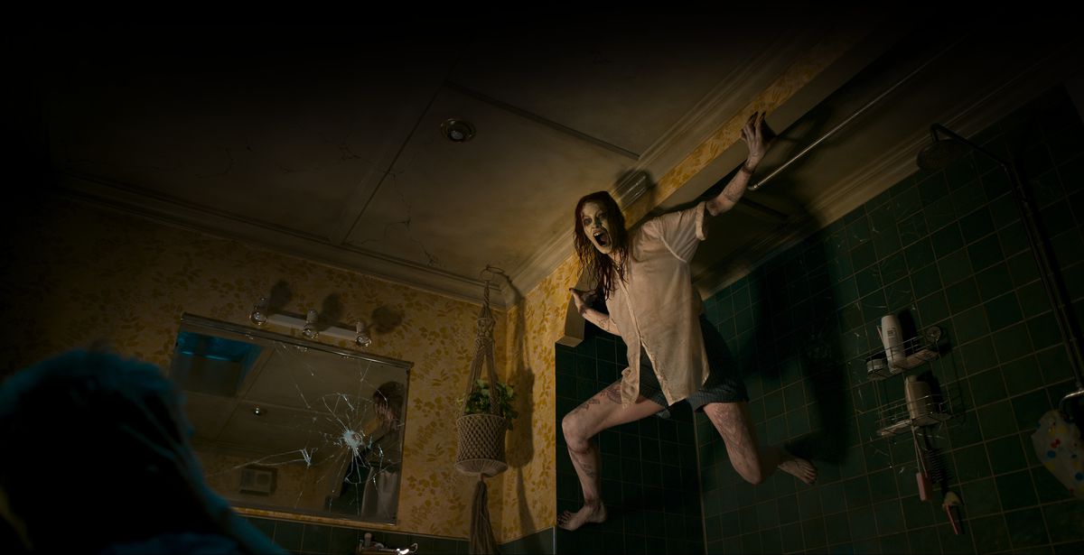 Newly possessed Deadite Ellie (Alyssa Sutherland) hisses through a blackened mouth while clinging to a wall in her dark apartment in Evil Dead Rise